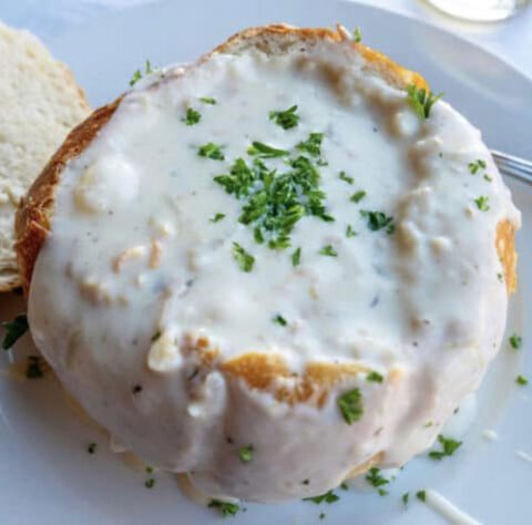 Top view of white clam chowder overflowing from a sourdough bread bowl