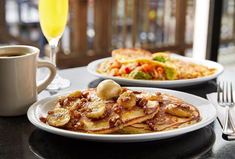 Plate of banana and pecan pancakes in the foreground with omelet dish in the background at Eagle Cafe, PIER 39, San Francisco