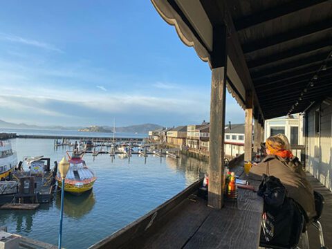 Two women at bar-style seating at the Eagle Cafe patio overlooking San Francisco Bay and pier area